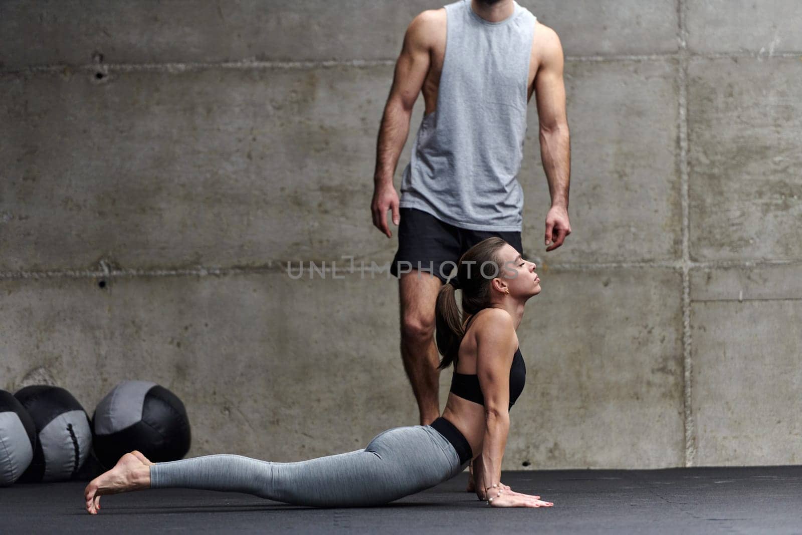 A muscular man assisting a fit woman in a modern gym as they engage in various body exercises and muscle stretches, showcasing their dedication to fitness and benefiting from teamwork and support by dotshock