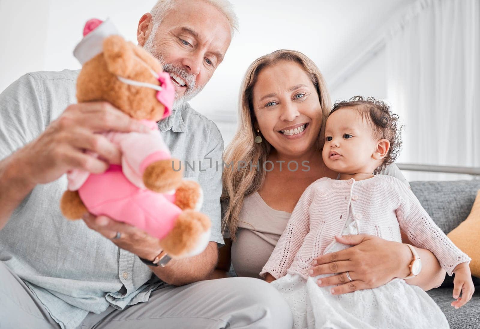 Mature, couple and baby with a toy while babysitting grand daughter with love, care and affection for fun playing. Caring, living room and grandfather, grandmother and child bonding with teddybear.