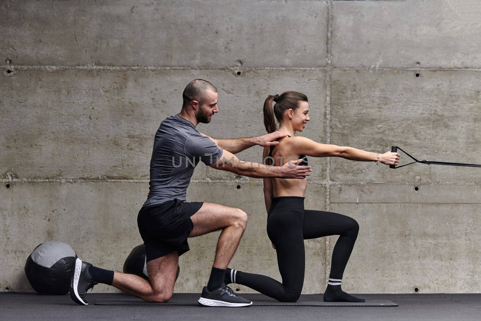 A muscular man assisting a fit woman in a modern gym as they engage in various body exercises and muscle stretches, showcasing their dedication to fitness and benefiting from teamwork and support.