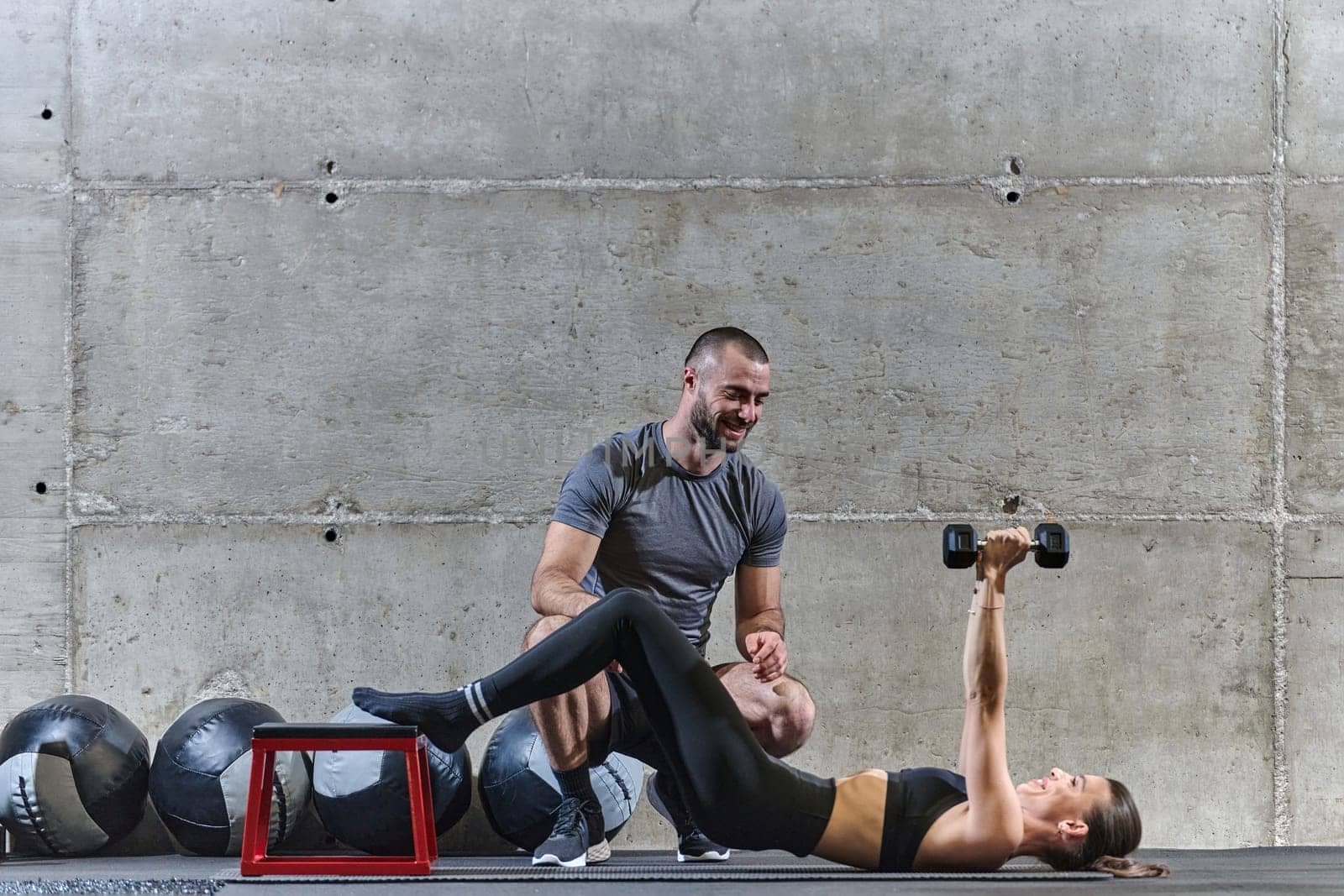 A muscular man assisting a fit woman in a modern gym as they engage in various body exercises and muscle stretches, showcasing their dedication to fitness and benefiting from teamwork and support by dotshock