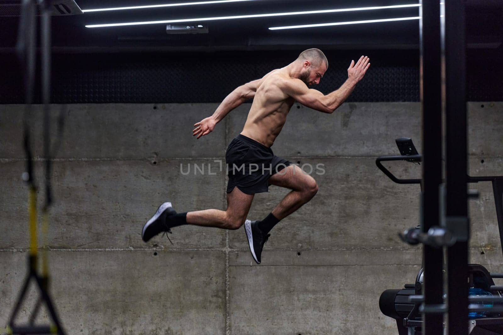 A muscular man captured in air as he jumps in a modern gym, showcasing his athleticism, power, and determination through a highintensity fitness routine.