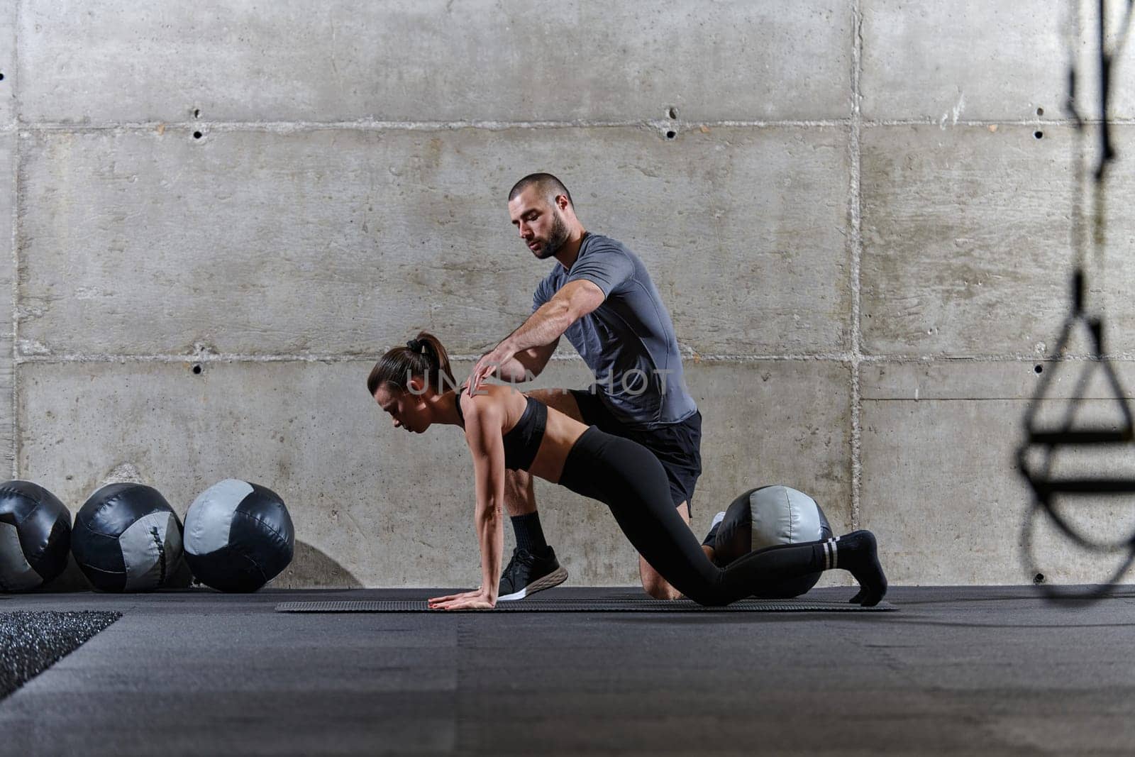 A muscular man assisting a fit woman in a modern gym as they engage in various body exercises and muscle stretches, showcasing their dedication to fitness and benefiting from teamwork and support.