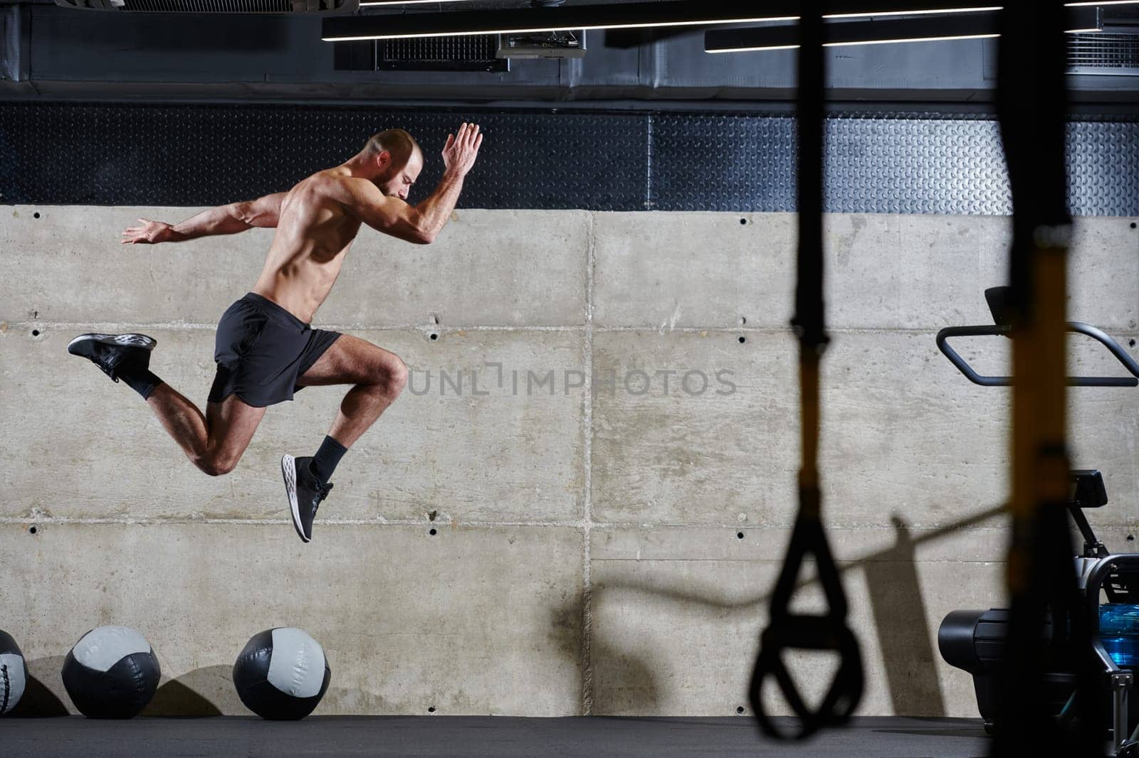 A muscular man captured in air as he jumps in a modern gym, showcasing his athleticism, power, and determination through a highintensity fitness routine.