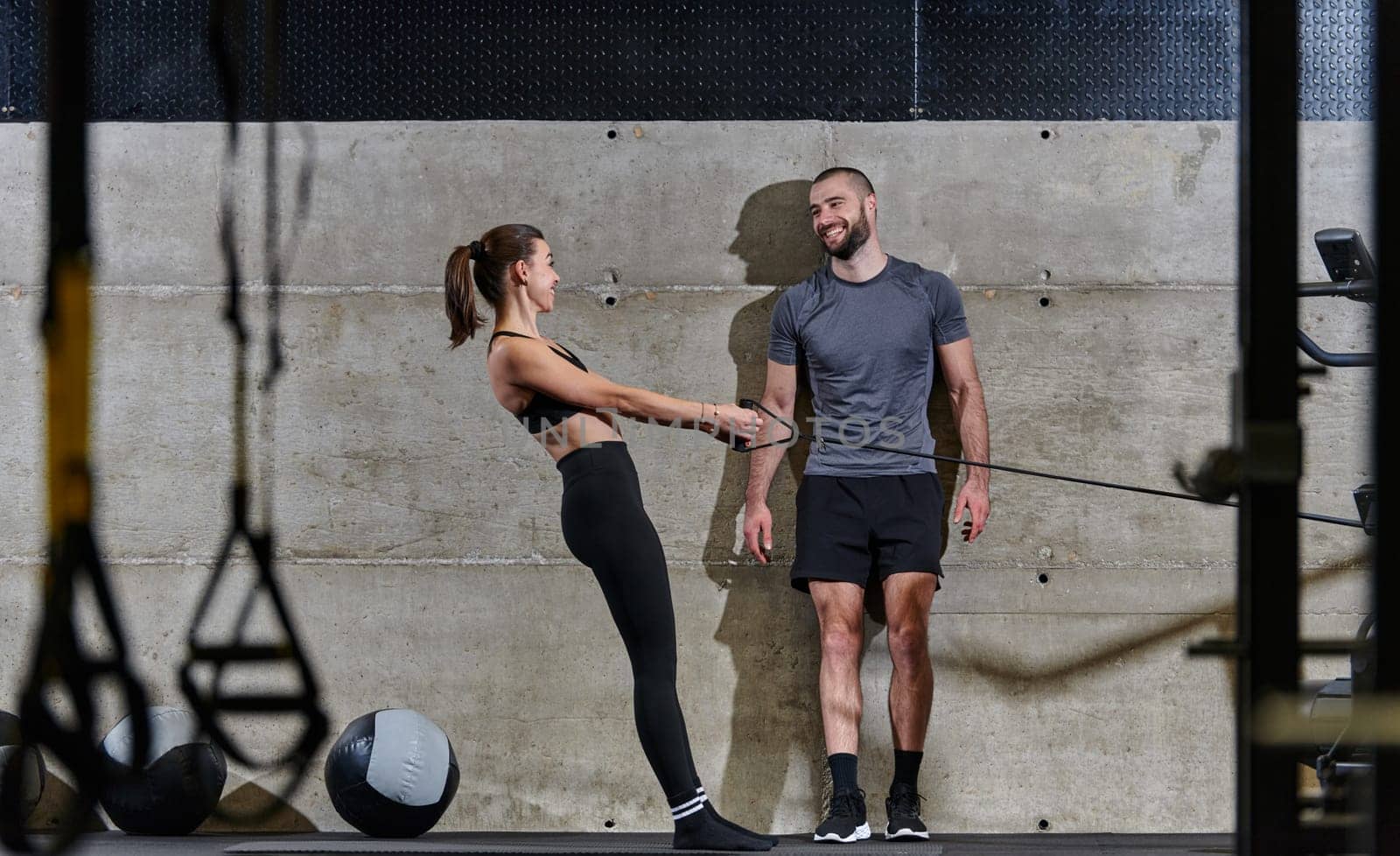 A muscular man assisting a fit woman in a modern gym as they engage in various body exercises and muscle stretches, showcasing their dedication to fitness and benefiting from teamwork and support by dotshock