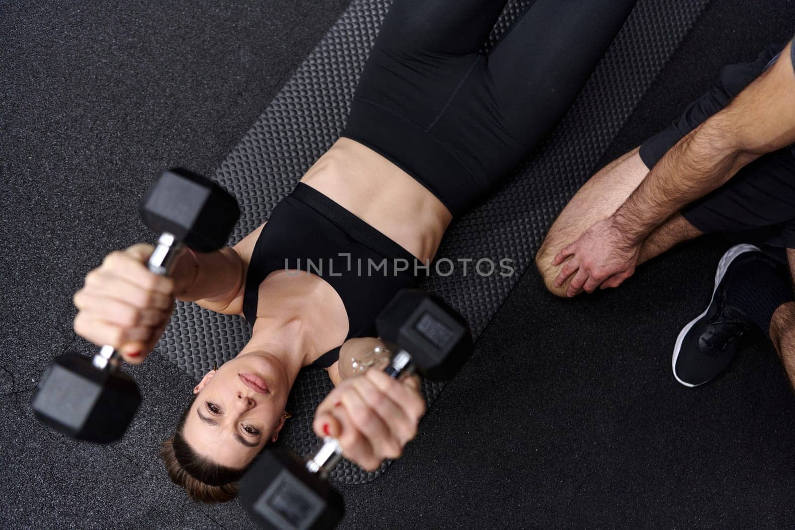 A muscular man assisting a fit woman in a modern gym as they engage in various body exercises and muscle stretches, showcasing their dedication to fitness and benefiting from teamwork and support.