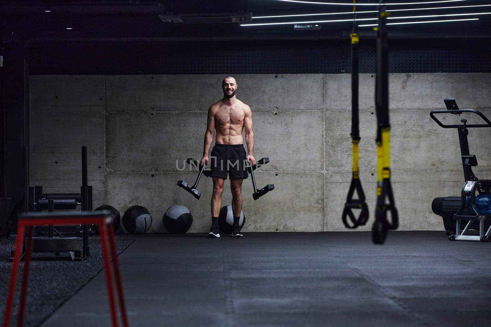 A muscular man performs shoulder exercises in a modern gym, showcasing his strength and dedication to fitness