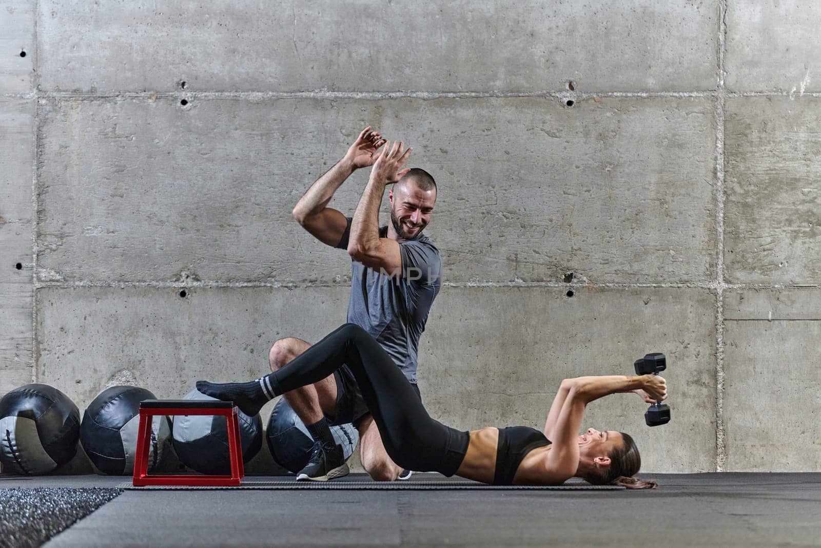 A muscular man assisting a fit woman in a modern gym as they engage in various body exercises and muscle stretches, showcasing their dedication to fitness and benefiting from teamwork and support.