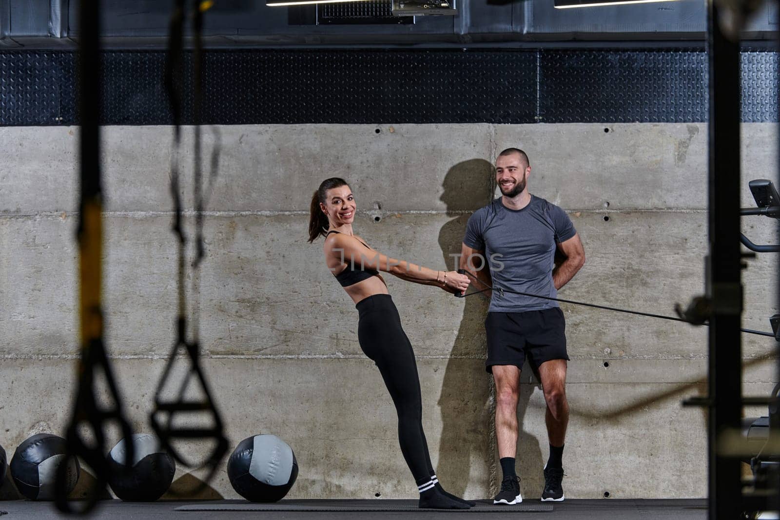 A muscular man assisting a fit woman in a modern gym as they engage in various body exercises and muscle stretches, showcasing their dedication to fitness and benefiting from teamwork and support by dotshock