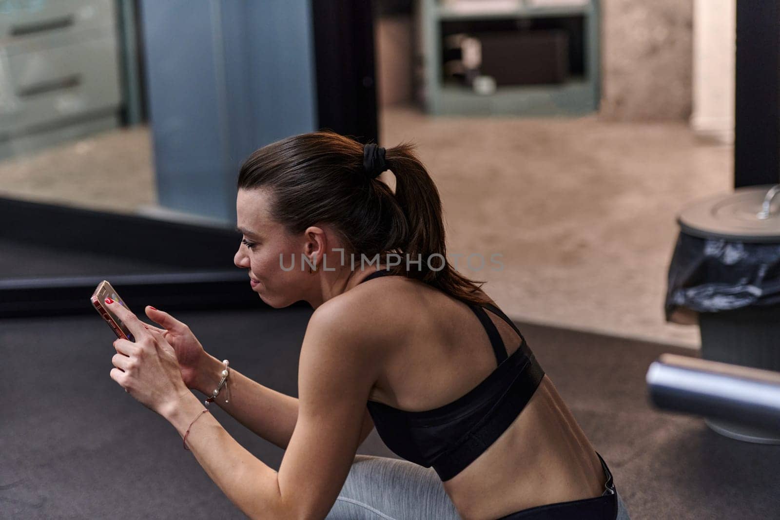 A fit woman in the gym taking a break from her training and uses her smartphone, embracing the convenience of technology to stay connected by dotshock