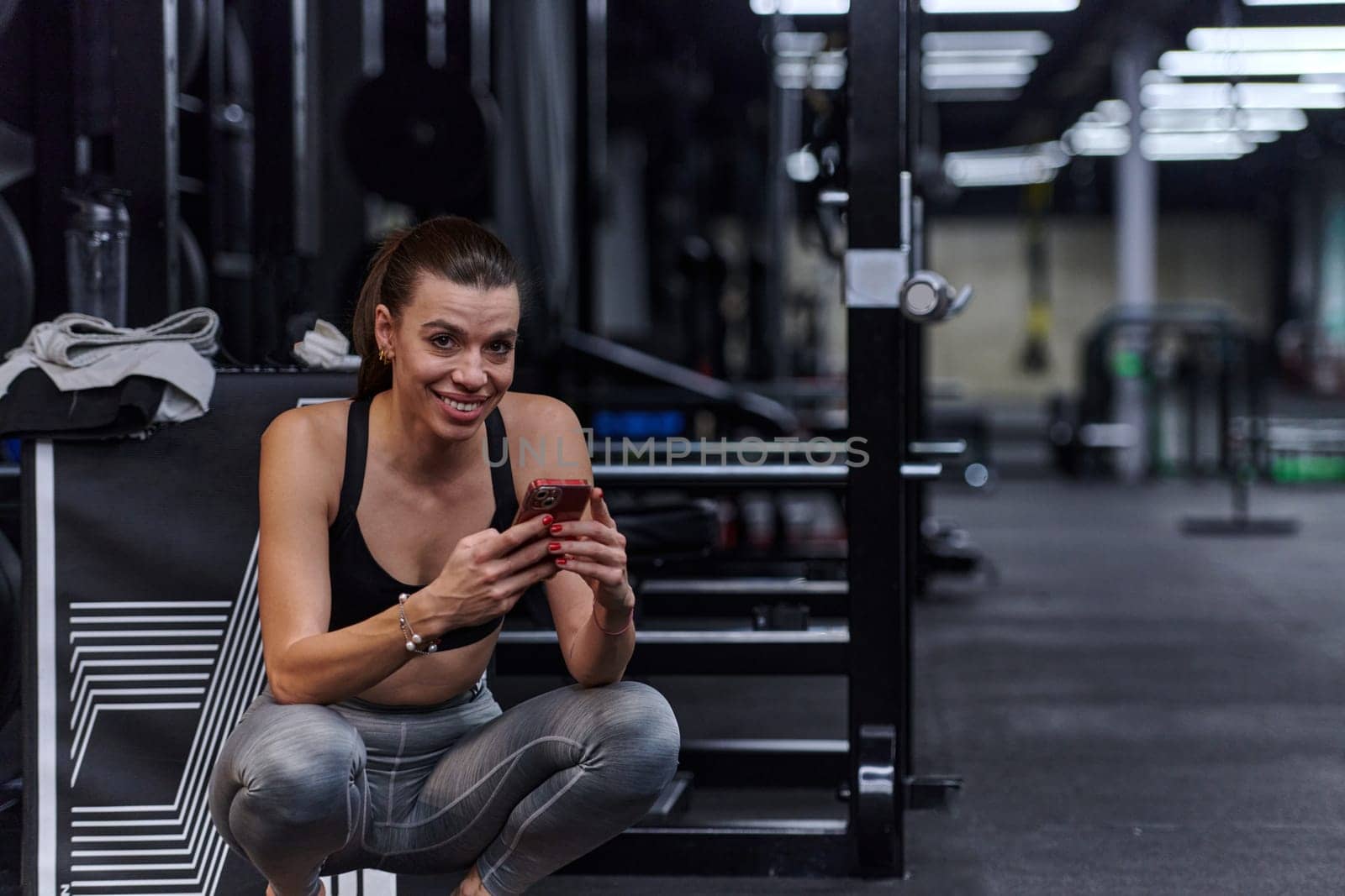 A fit woman in the gym taking a break from her training and uses her smartphone, embracing the convenience of technology to stay connected by dotshock