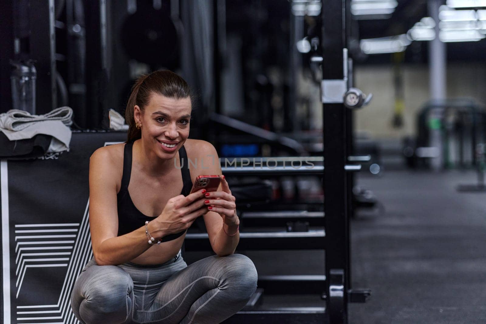 A fit woman in the gym taking a break from her training and uses her smartphone, embracing the convenience of technology to stay connected.