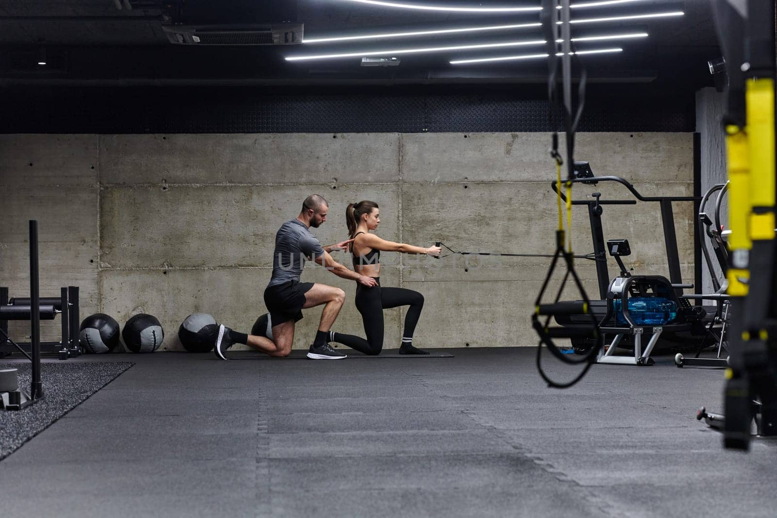 A muscular man assisting a fit woman in a modern gym as they engage in various body exercises and muscle stretches, showcasing their dedication to fitness and benefiting from teamwork and support.