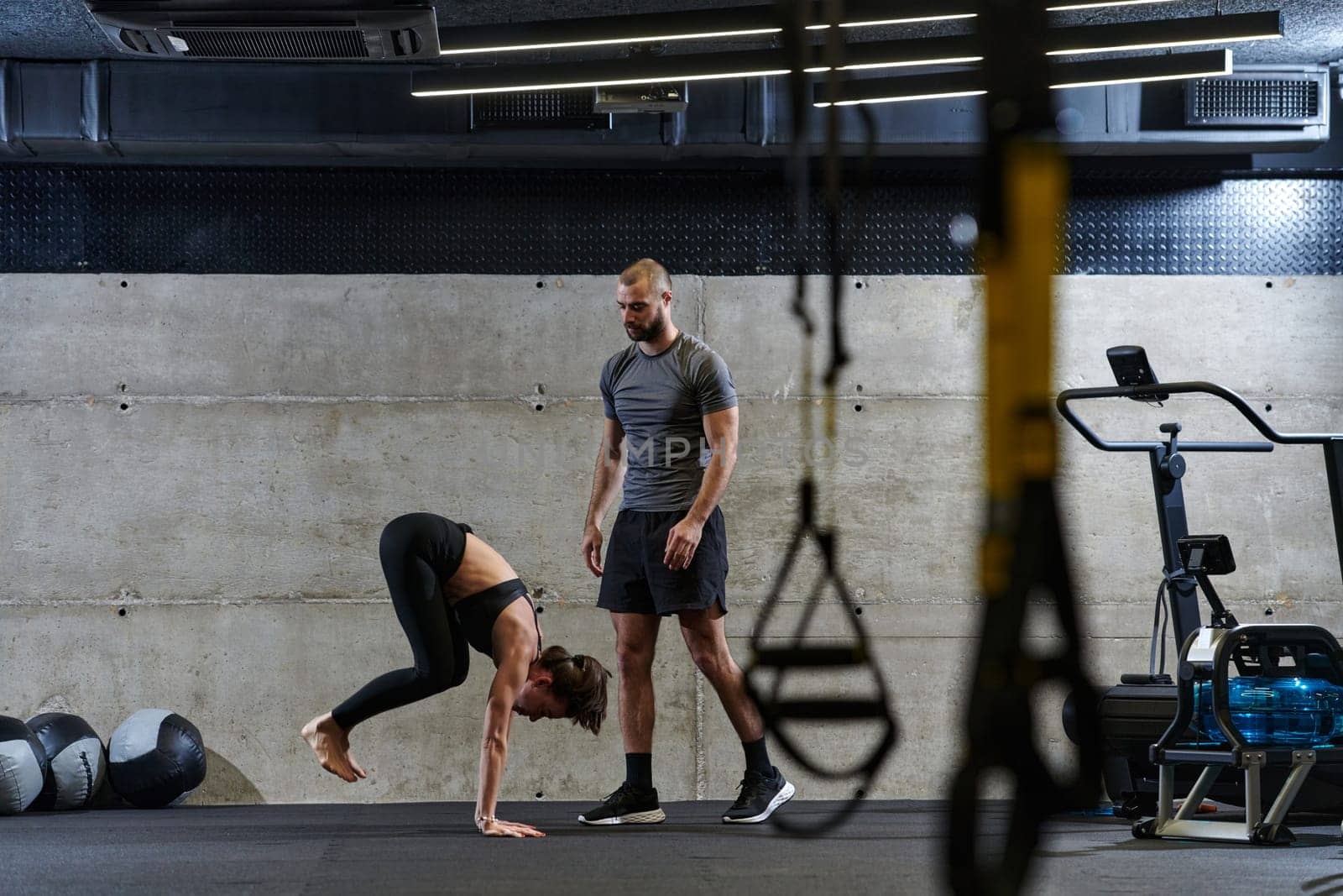 A muscular man assisting a fit woman in a modern gym as they engage in various body exercises and muscle stretches, showcasing their dedication to fitness and benefiting from teamwork and support.