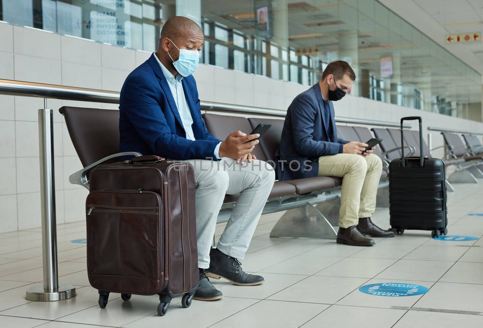 Social distance, suitcase and businessmen waiting in the airport and networking with cellphone. Face mask, luggage and professional male employees sitting with travel restrictions browsing on a phone.