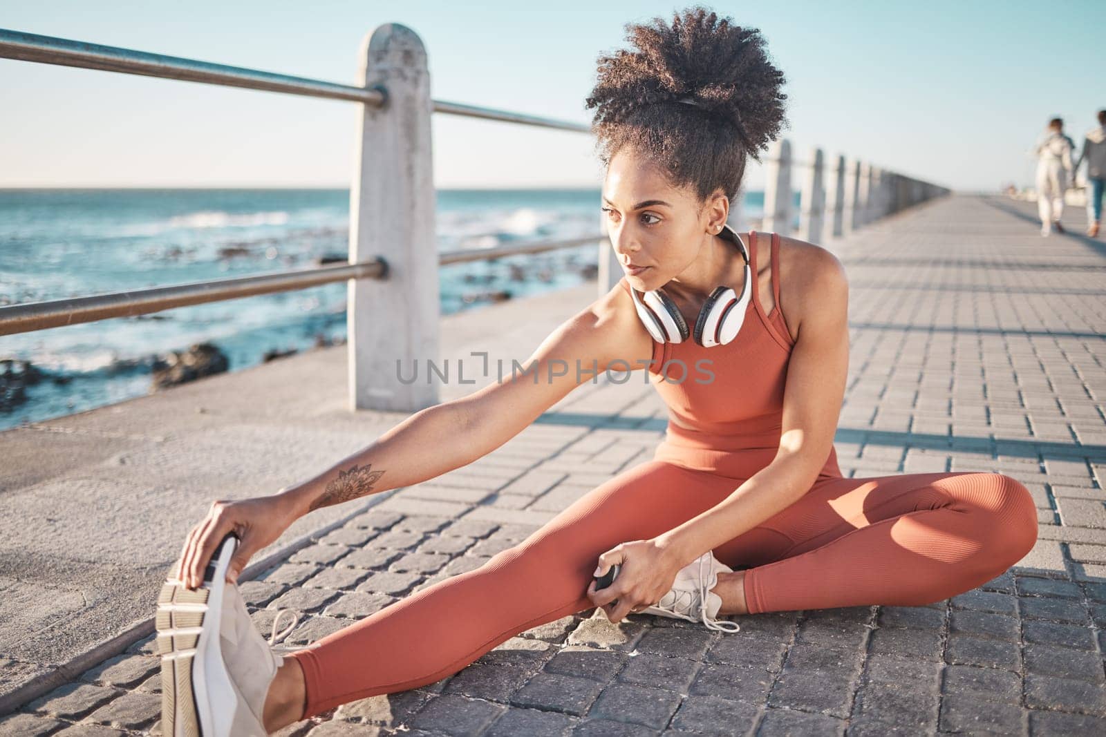 Black woman, seaside and stretching for workout, training and exercise for wellness, energy and health. African American female, girl and athlete stretch legs, promenade and fitness for stress relief by YuriArcurs