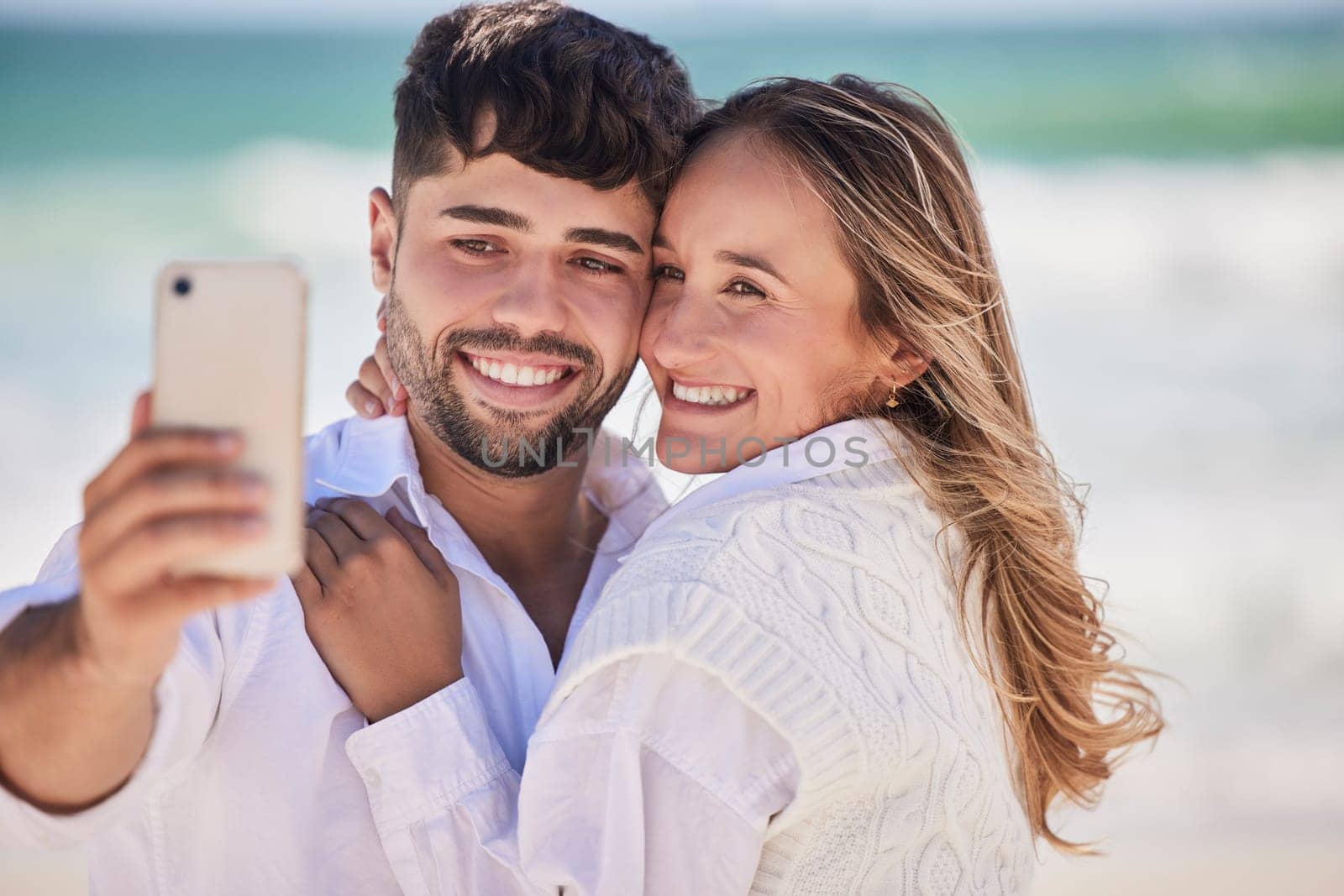 Beach, love and happy couple taking a selfie while on a date for valentines day, romance or anniversary. Happiness, smile and young man and woman hugging while taking picture by the ocean on vacation.