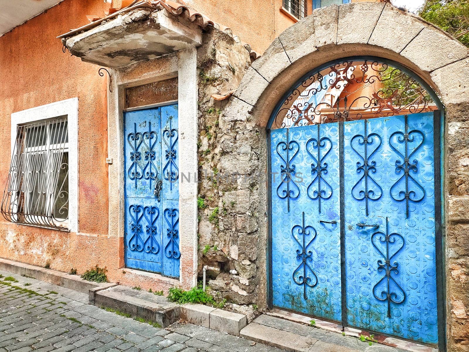 Facade of old village house with blue door and gate, with patterned forging