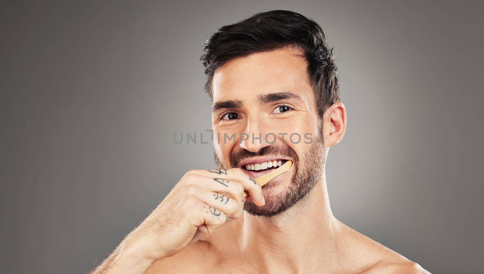 Man, brushing teeth and dental healthcare for beauty smile or grooming morning routine with toothbrush in studio. Face, smile and hygiene health with model cleaning teeth portrait in grey background by YuriArcurs