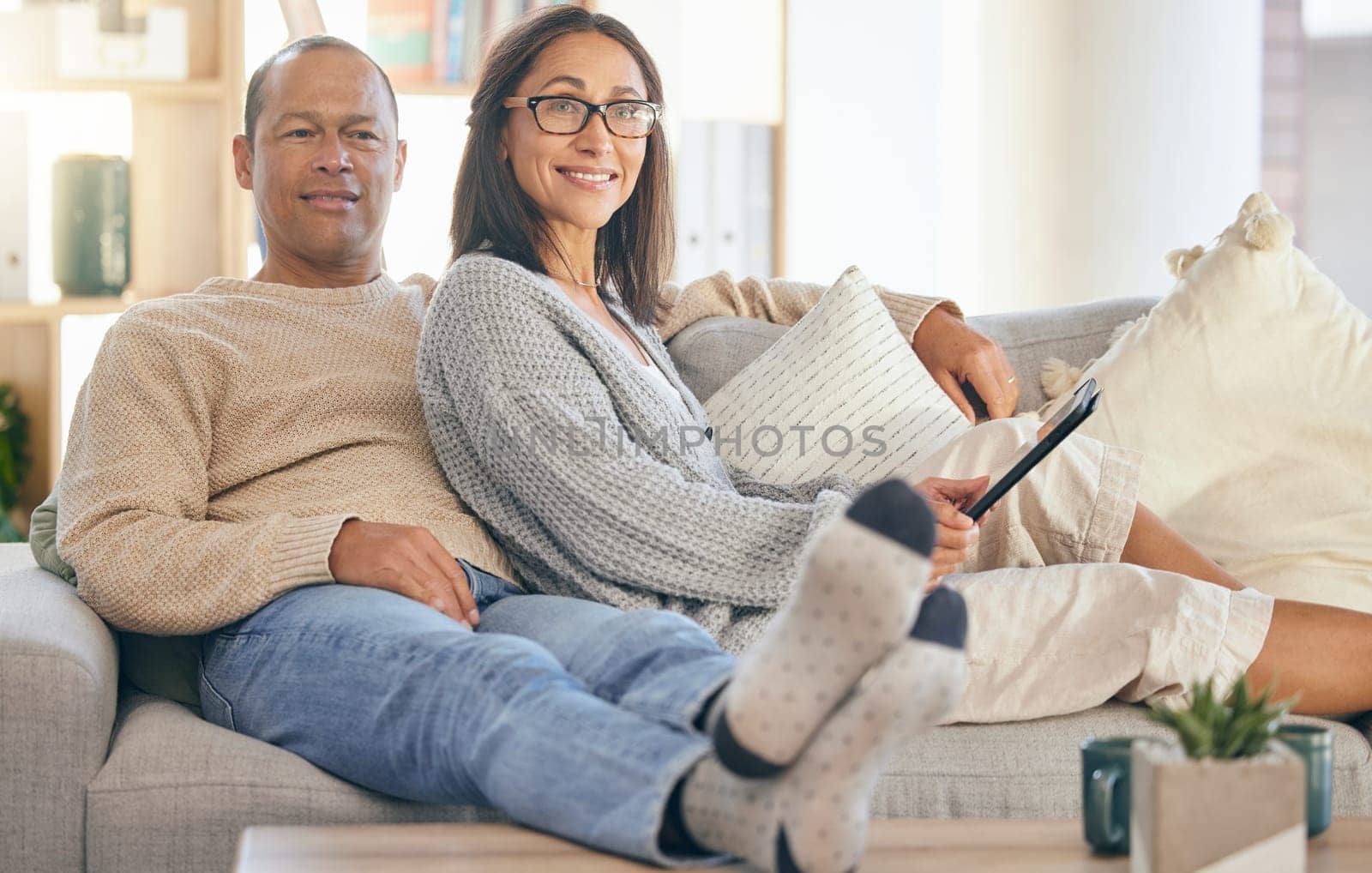 Mature couple, tablet and relax portrait on sofa together for love, support and romance bonding in living room at home. Man smile, happy woman, and romantic quality time on couch with tech device by YuriArcurs