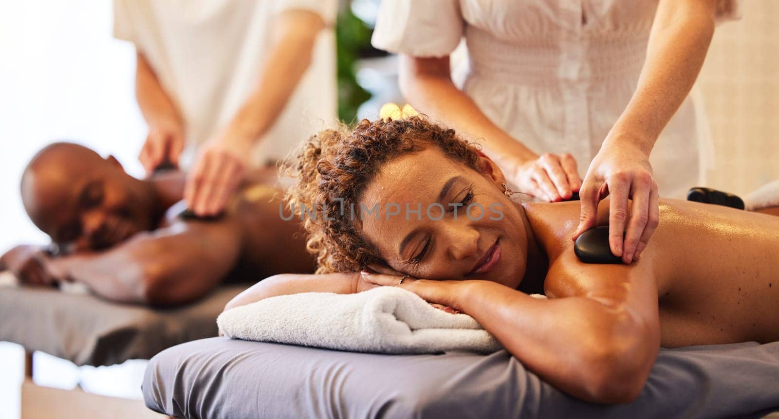 Spa, wellness and massage for couple and hot stone therapy, massage therapist hands for stress relief and body health. Man and woman relax with luxury service at beauty salon, peace and detox release by YuriArcurs