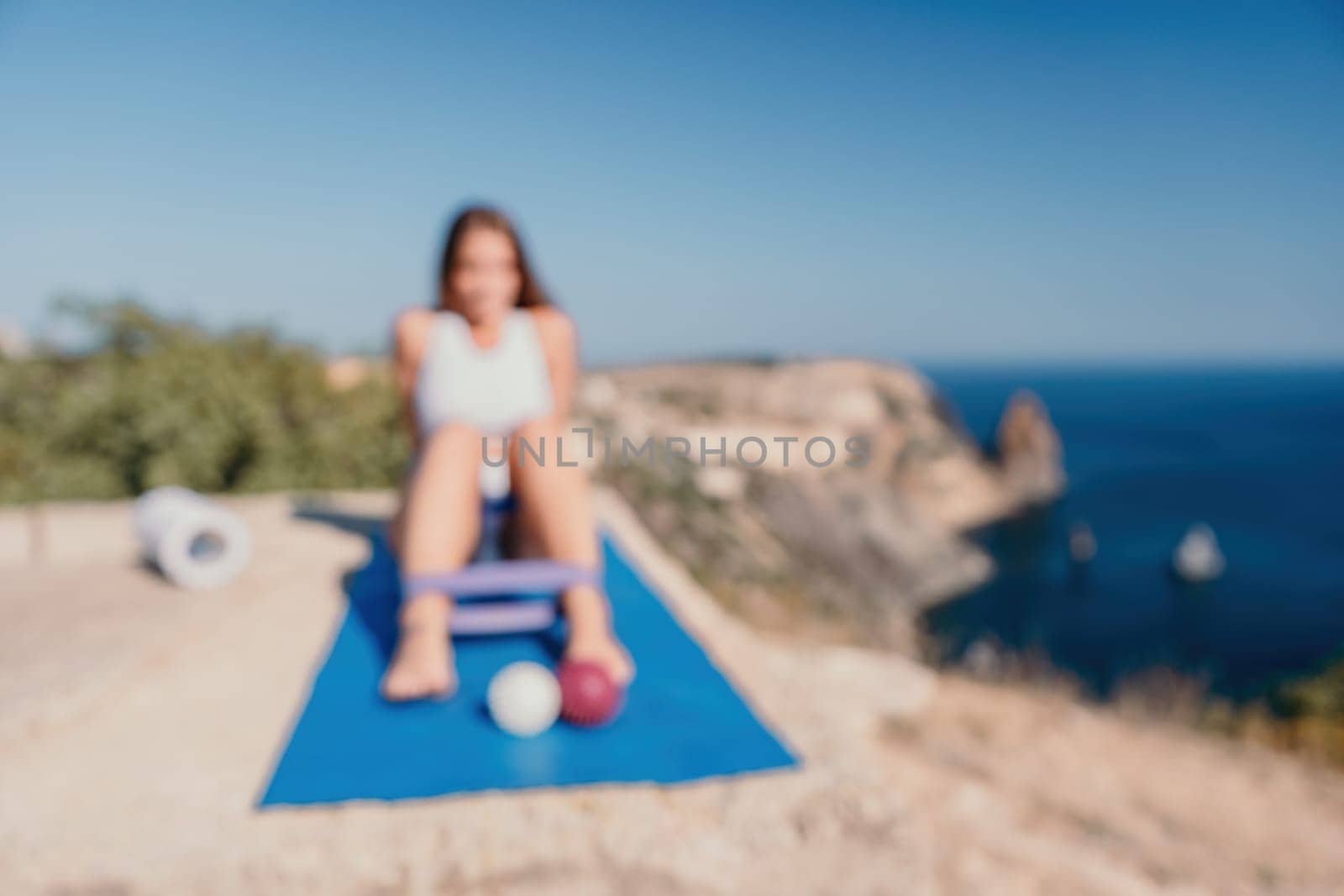 Abstract defocused Woman sea pilates. Sporty happy woman practicing fitness on yoga mat with rubber band, massage balls and roller near sea, active female outside, enjoying healthy lifestyle by panophotograph