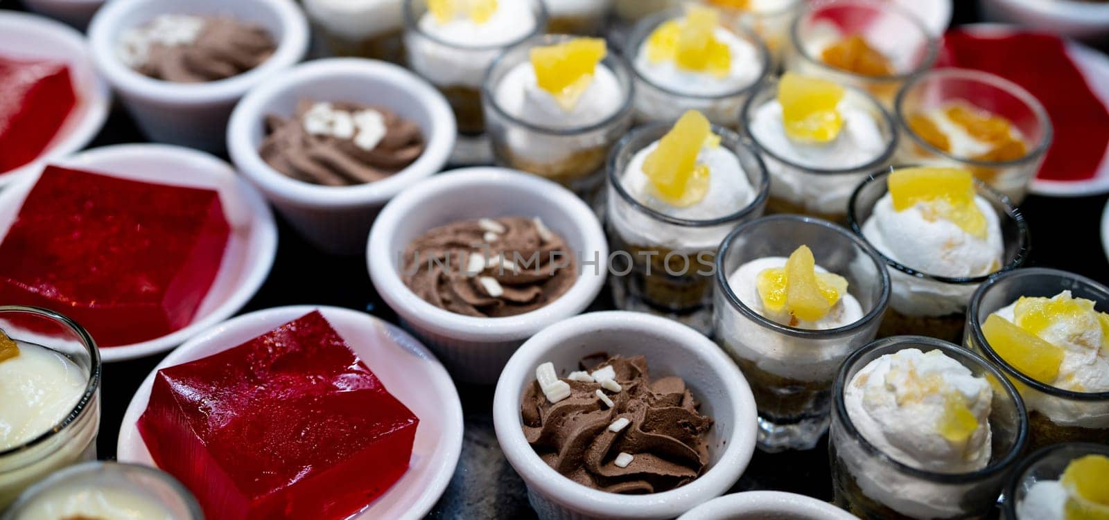 Dessert buffet catering concept. Selective focus dessert on buffet counter. Dessert in plate, cup, and glass on table at restaurant for lunch buffet. Sweet food. Red jelly agar, chocolate mousse. by Fahroni