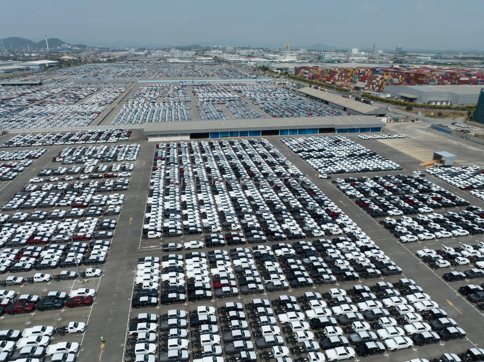 Aerial view of new cars stock at factory parking lot. Above view cars parked in a row. Automotive industry. Logistics business. Import or export new cars at warehouse. Big parking lot at port terminal