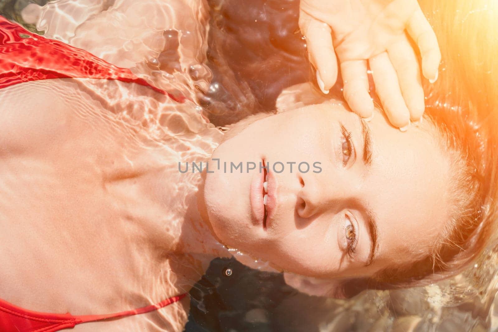 Woman travel portrait. close-up portrait of a happy woman with long hair in a red bikini, floating in water and smiling at the camera. by panophotograph