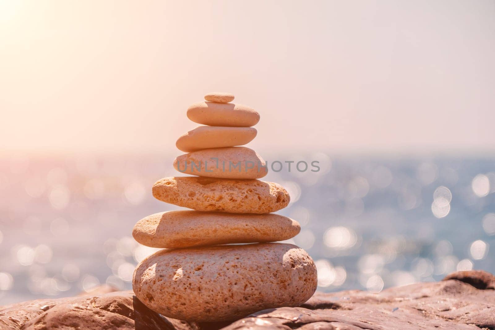 Balanced Pebbles Pyramid on the Beach on Sunny Day and Clear Sky at Sunset. Blue Sea on Background Selective focus, zen stones on sea beach, meditation, spa, harmony, calm, balance concept.