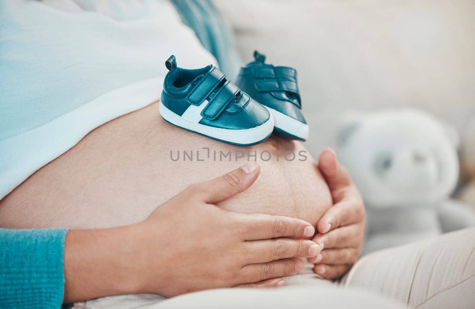 Mother with pregnant stomach in hands, shoes for baby with pregnancy, relax and waiting for birth with love and hope for healthy child. Woman, prenatal care and mom at family home, ready for newborn