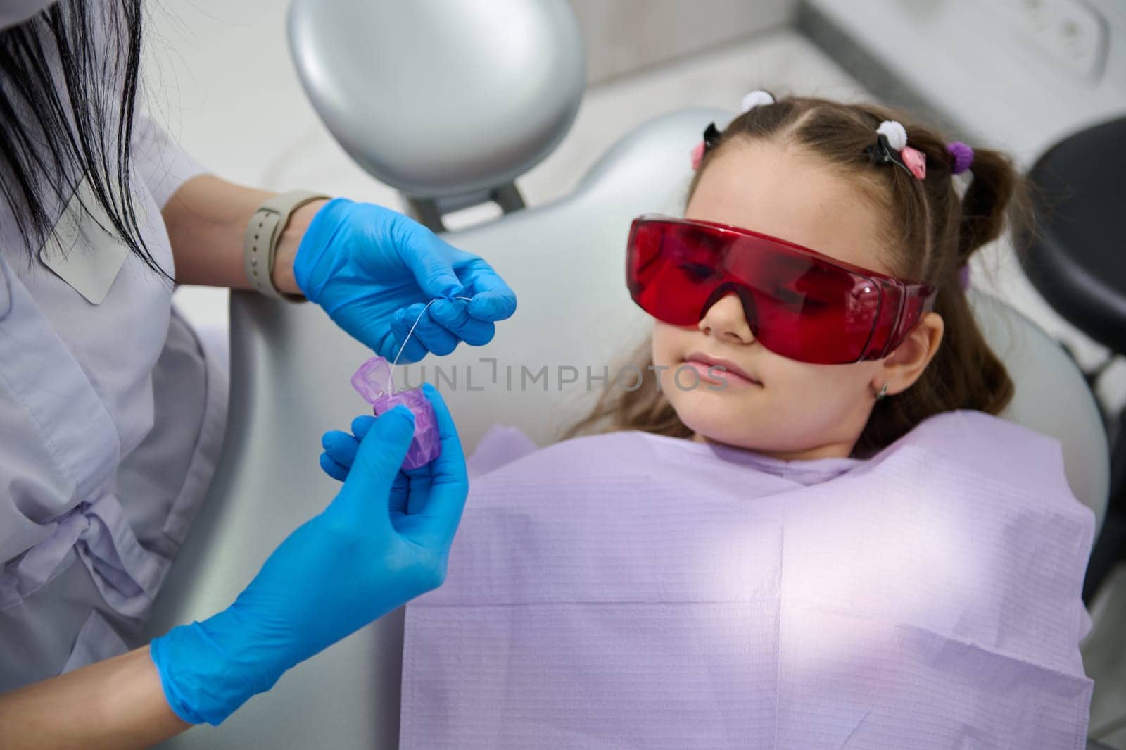 Cute child girl listens to a dental hygienist explaining how to clean teeth using a dental floss after teeth brushing by artgf