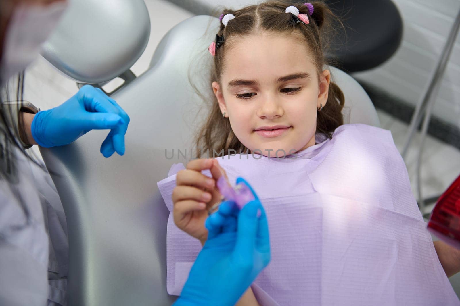 Close-up portrait of a beautiful Middle-Eastern little child girl at dentist's appointment, holding dental floss, getting teeth check-up in pediatric dentistry clinic. Dental care and hygiene concept