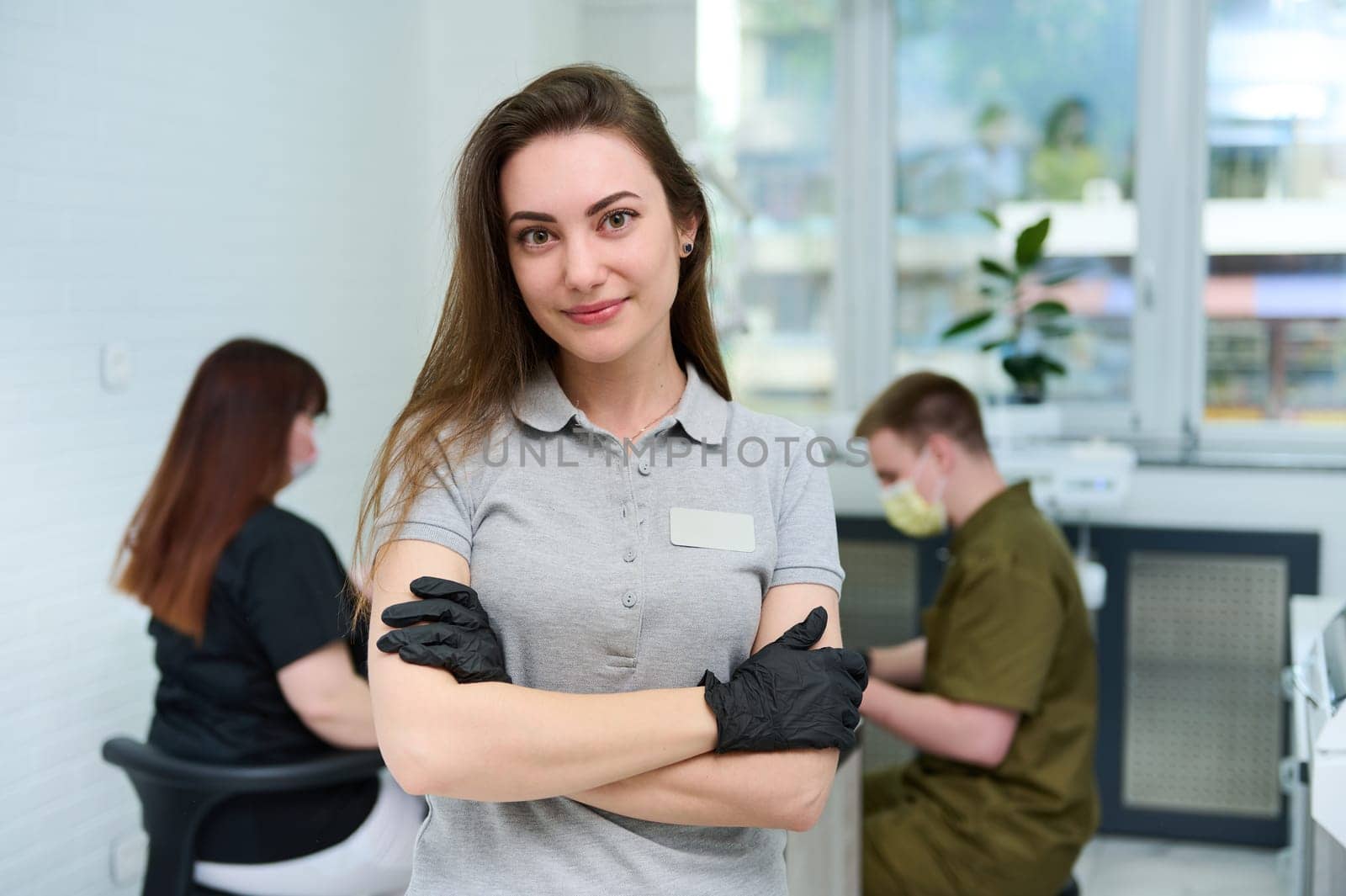 Caucasian successful committed young female dentist doctor looking at camera, standing with arms folded in dental office by artgf