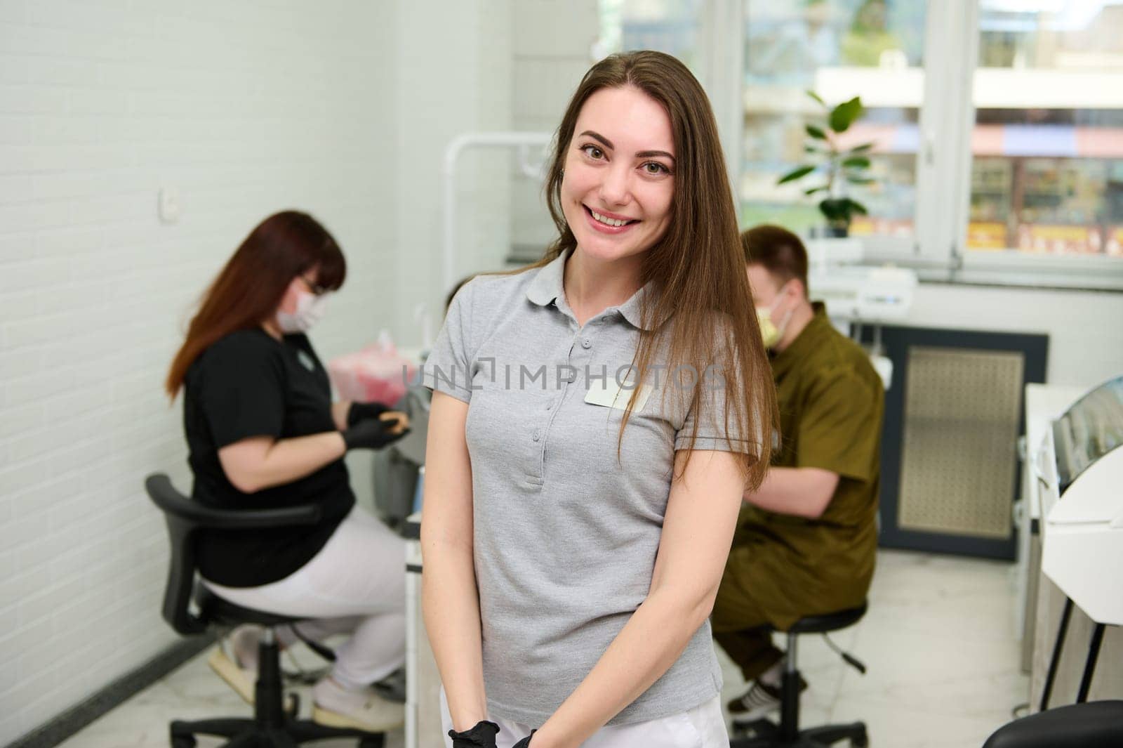 Portrait of Caucasian young female dentist doctor, dental hygienist, maxillofacial surgeon, orthodontist smiling looking at camera, standing in the dental examination room of a modern dentistry clinic