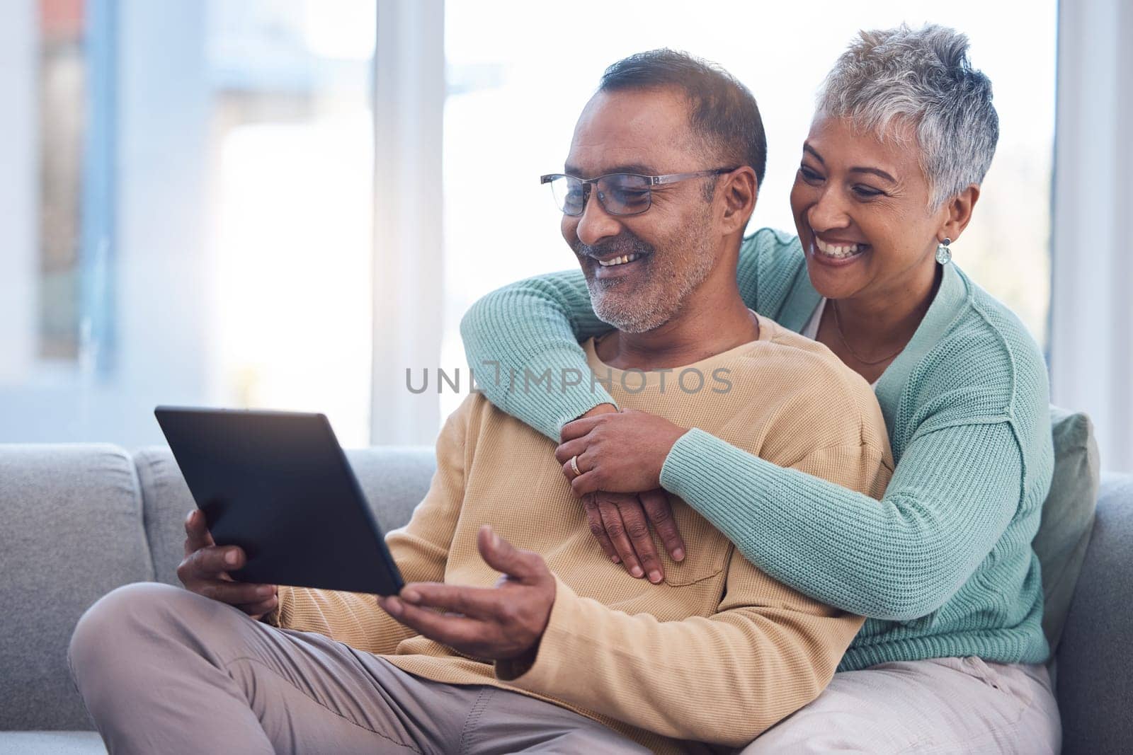 Old couple, tablet and relax with hug on sofa, social media or streaming movie. Love, retirement and elderly man and woman hugging or embrace on couch in living room while internet browsing on tech. by YuriArcurs