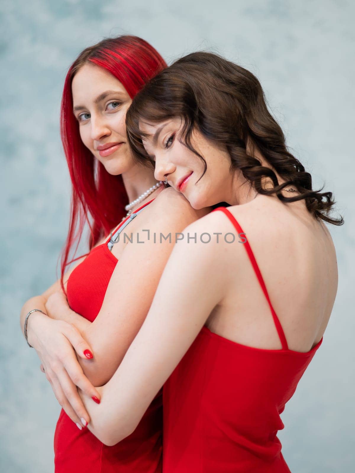 A close-up portrait of two tenderly embracing women dressed in identical red dresses. Lesbian intimacy. by mrwed54