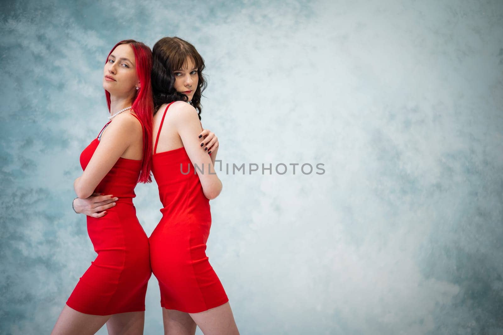 Portrait of two women dressed in identical red dresses and standing back to back. Lesbian intimacy