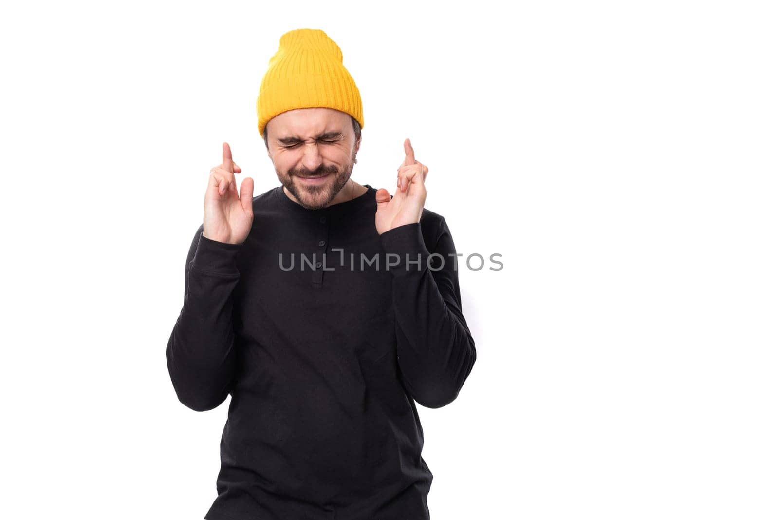 hopeful 30s authentic brunet male adult in black sweatshirt praying on white background with copy space.