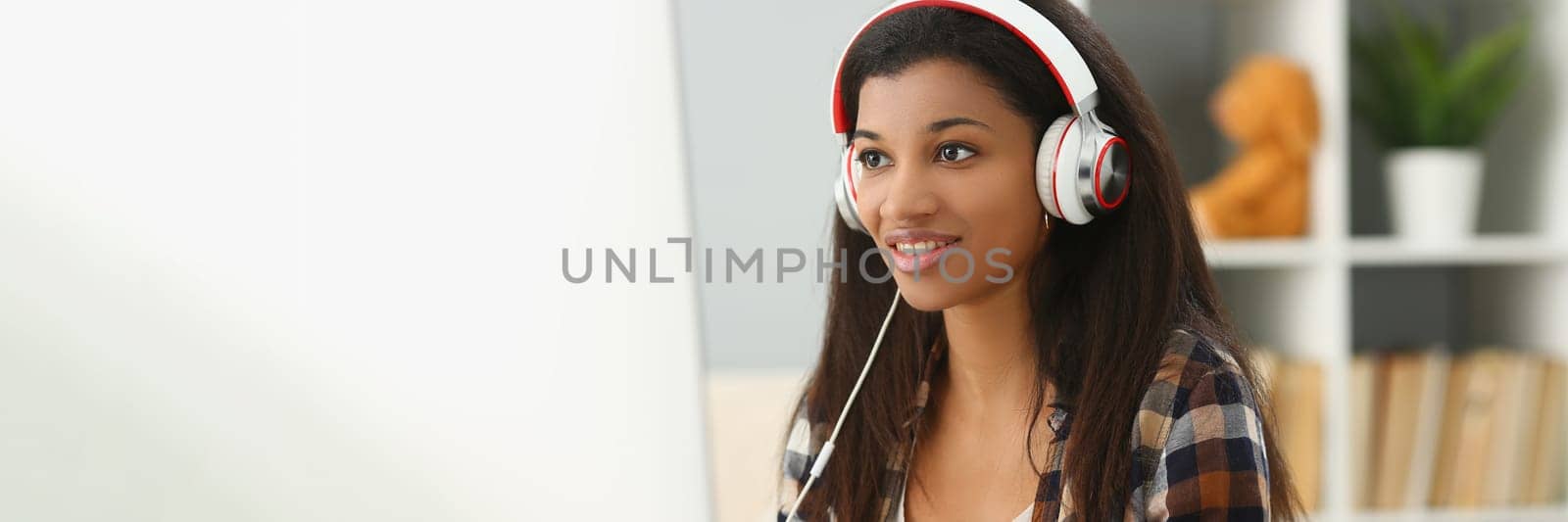 Smiling young black woman in headphones sitting at desk by kuprevich