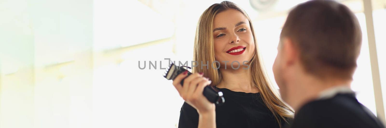 Smiling female hairdresser holding hair trimmer and communicating with male client. Choosing stylish fashionable hairstyle for man