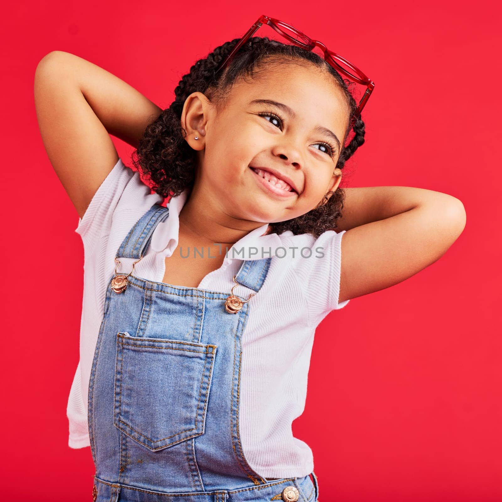 Little girl, happy and thinking in fashion pose, trendy or cool style clothes on isolated red background for kids branding. Smile, youth and child stretching arms in playful, funny and goofy posing.