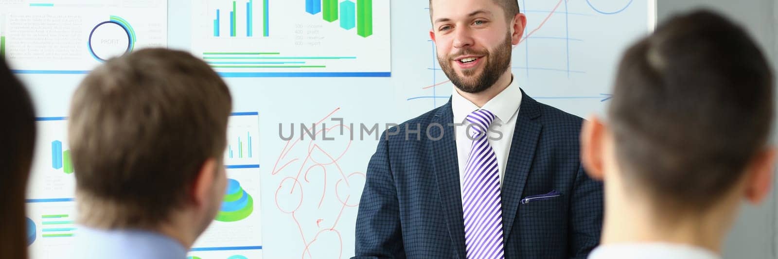 Male business coach speaker in suit makes presentation on white board. Male speaker advising on training and persuading client group employees