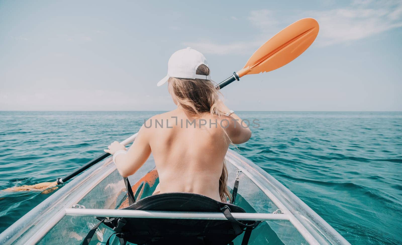 Woman in kayak back view. Happy young woman with long hair floating in transparent kayak on the crystal clear sea. Summer holiday vacation and cheerful female people relaxing having fun on the boat by panophotograph