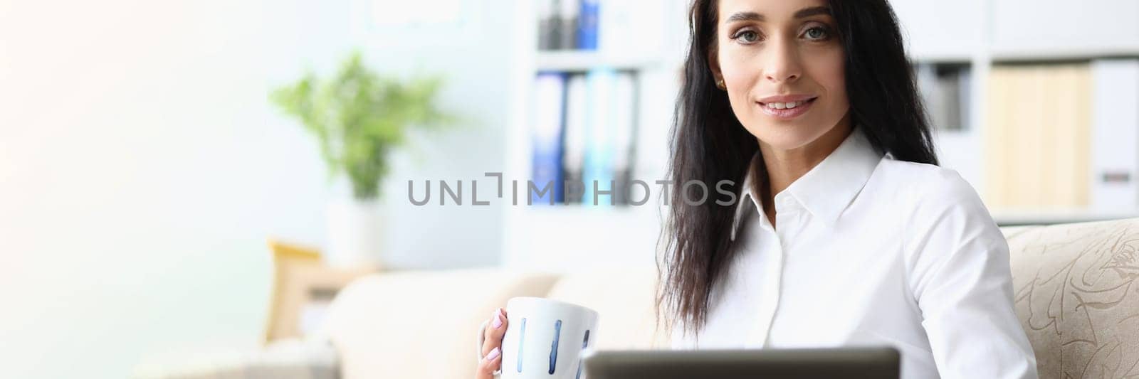 Portrait of a beautiful woman with tablet and cup on sofa. Applications for business and planning the working day