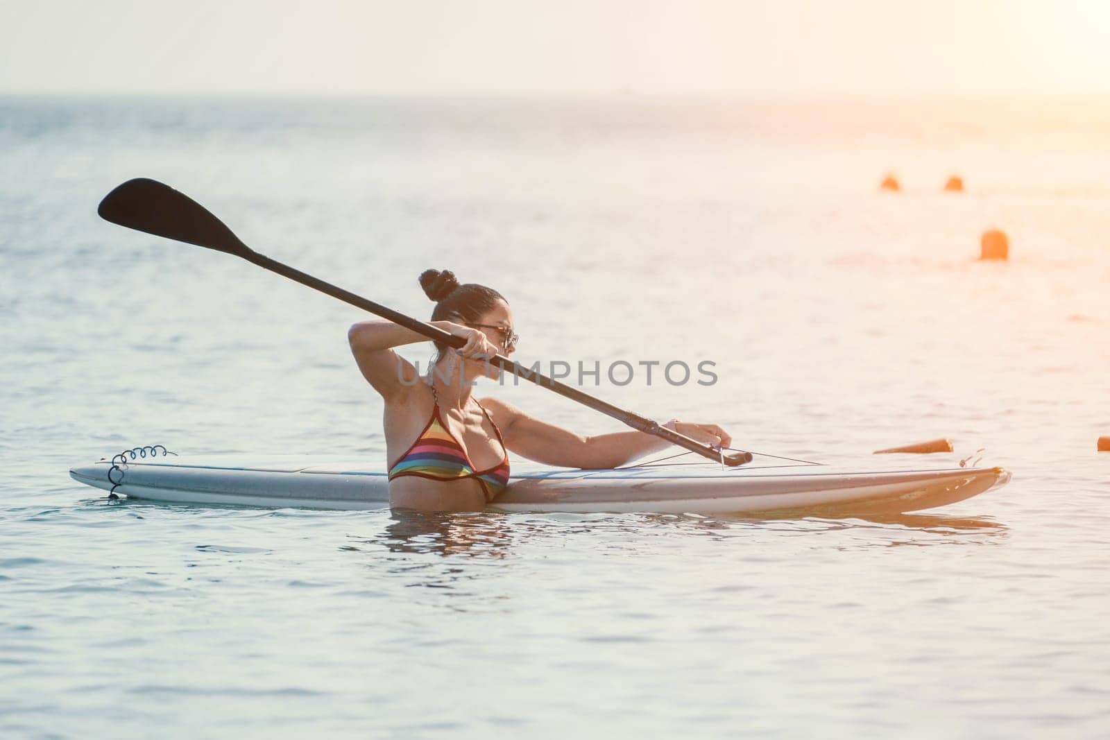 Sea woman sup. Silhouette of happy middle aged woman in rainbow bikini, surfing on SUP board, confident paddling through water surface. Idyllic sunset. Active lifestyle at sea or river