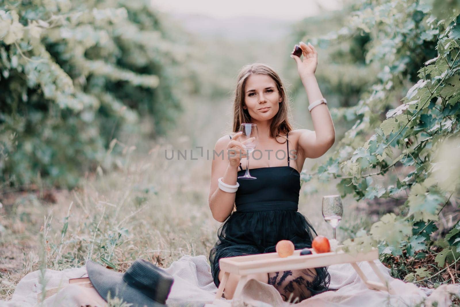 Woman picnic vineyard. Happy woman with a glass of wine at a picnic in the vineyard, wine tasting at sunset and open nature in the summer. Romantic dinner, fruit and wine. by panophotograph