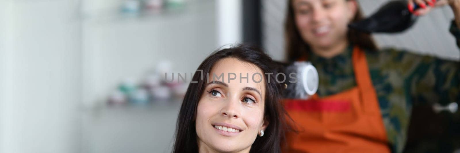 Hairdresser drying hair woman client in hairdressing beauty salon. Hair styling in beauty salon