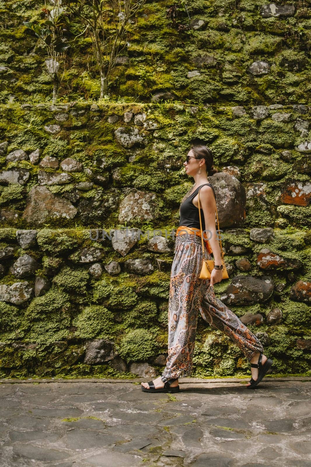 Walking young stylish girl on temple wall background. Puru Gunung Kawi ancient architecture, female tourist in rocky temple
