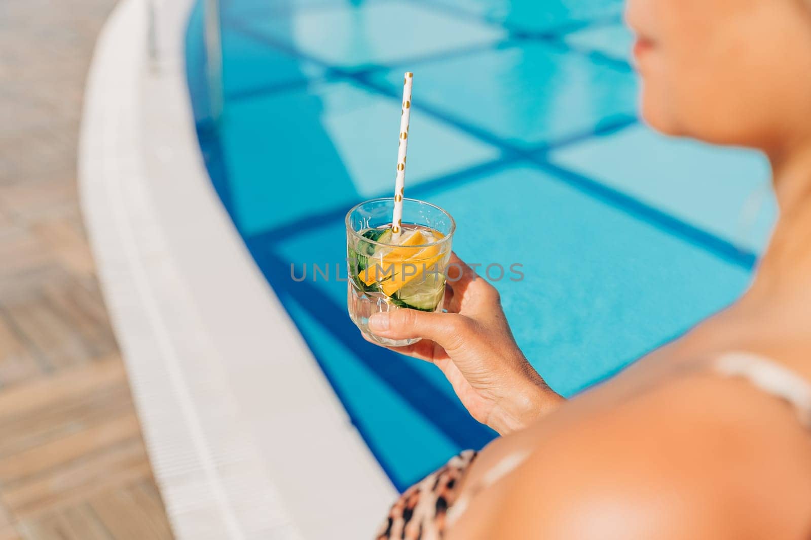 Close up of mature adult woman holding cocktail and relaxing near the pool. Beautiful elegant caucasian senior woman drink lemonade cocktail enjoying summer vacation by Ostanina