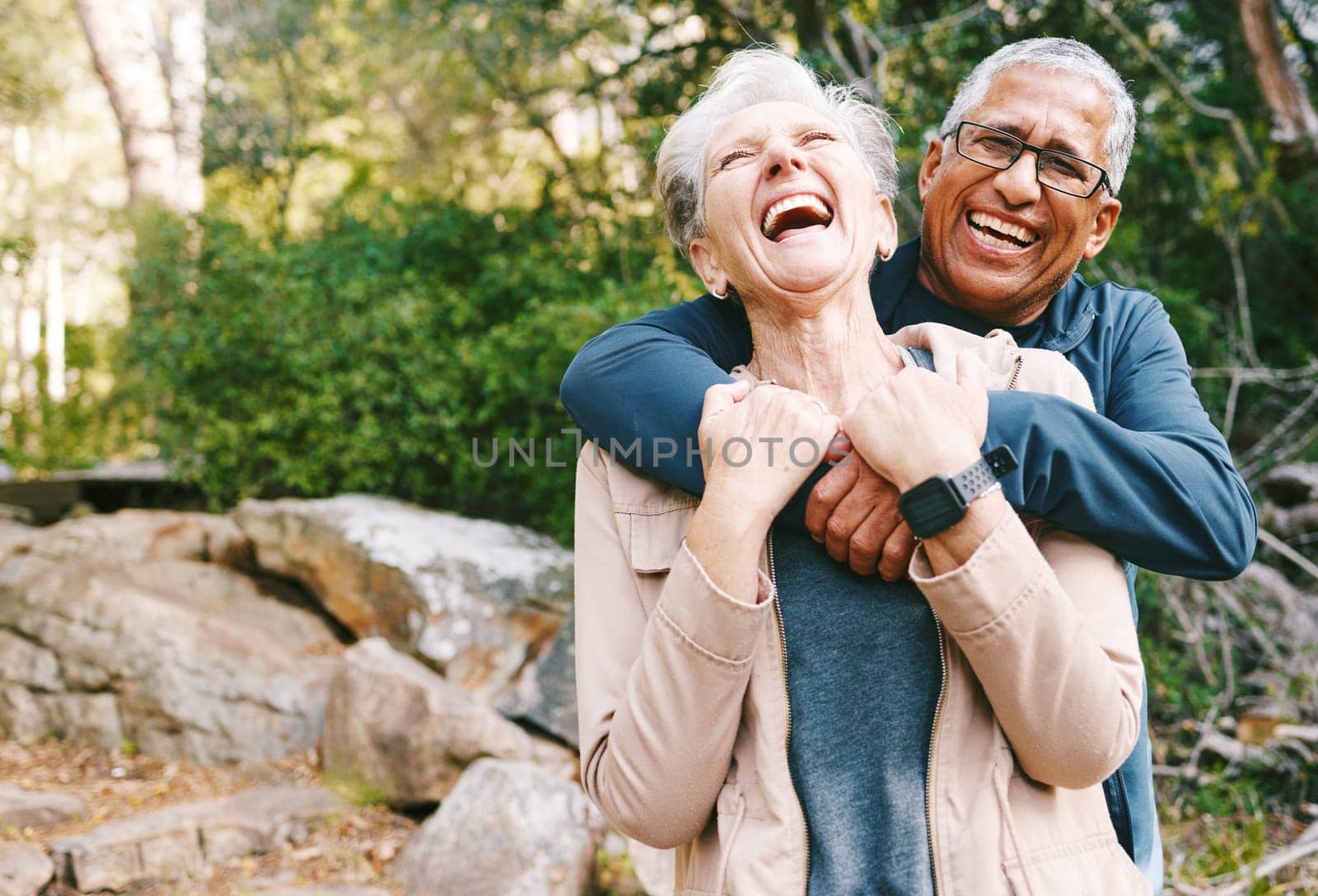Hiking, laugh and romance with a senior couple hugging while in the woods or nature forest together in summer for a hike. Fun, joke and bonding with a mature man and woman enjoying retirement outdoor.